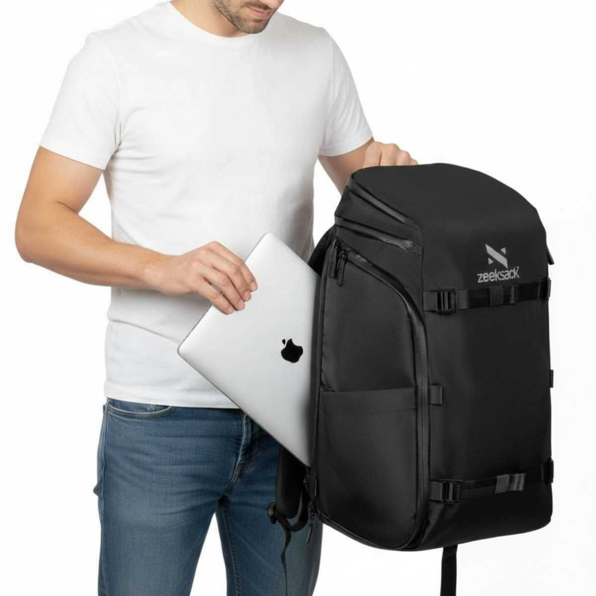 Mies valkoisessa t-paidassa laittaa hopeisen kannettavan tietokoneen mustaan reppuun.