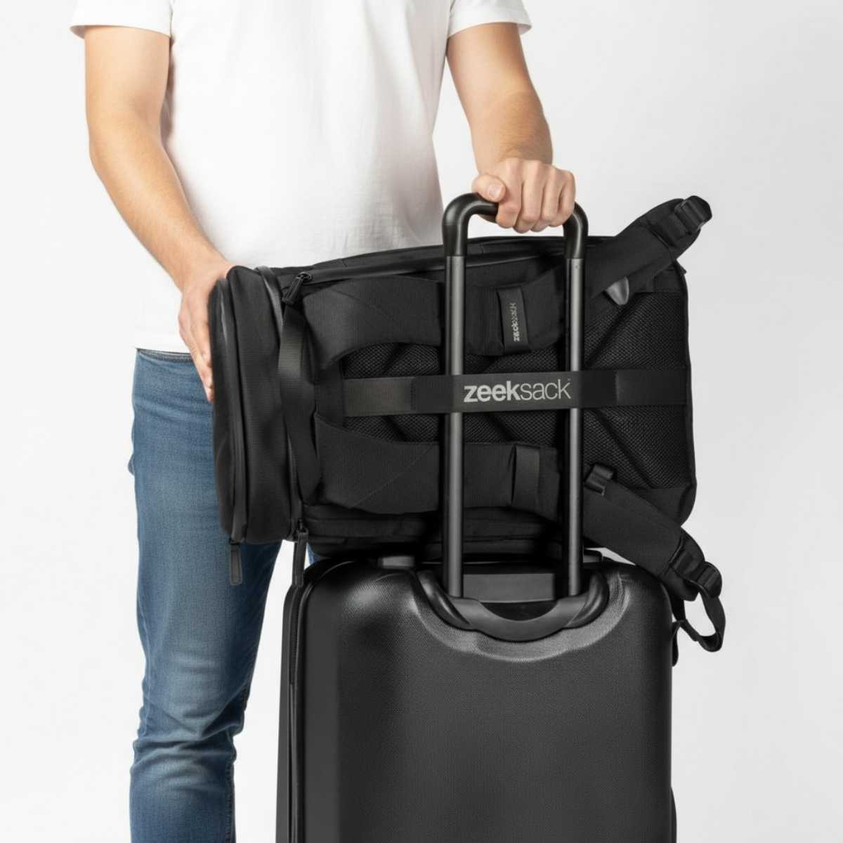 Mies valkoisessa t-paidassa ja farkuissa asettaa mustan repun harmaan matkalaukun päälle.