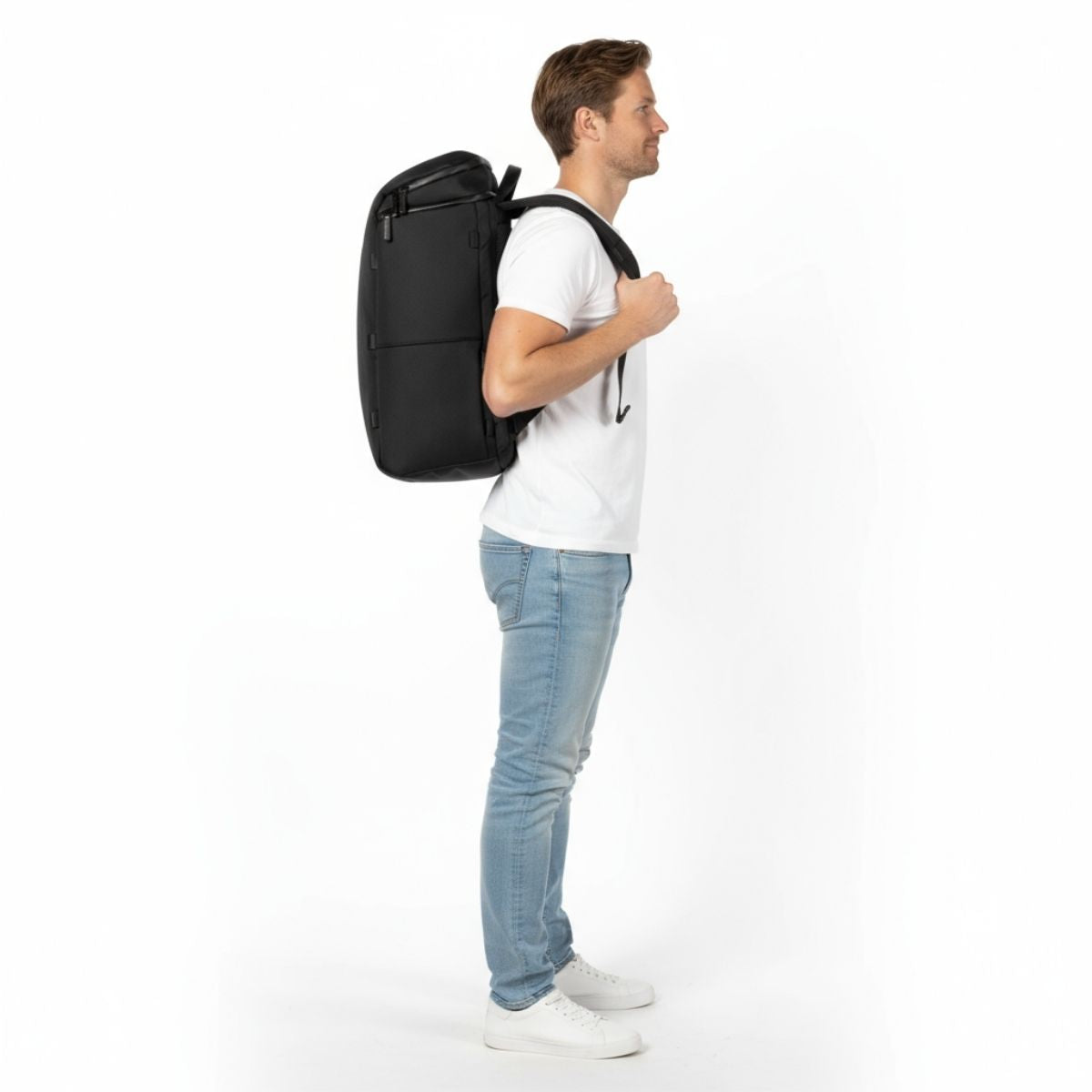 Mies valkoisessa t-paidassa ja farkuissa kantaa mustaa Zeeksack-reppua, sivulta nähtynä.