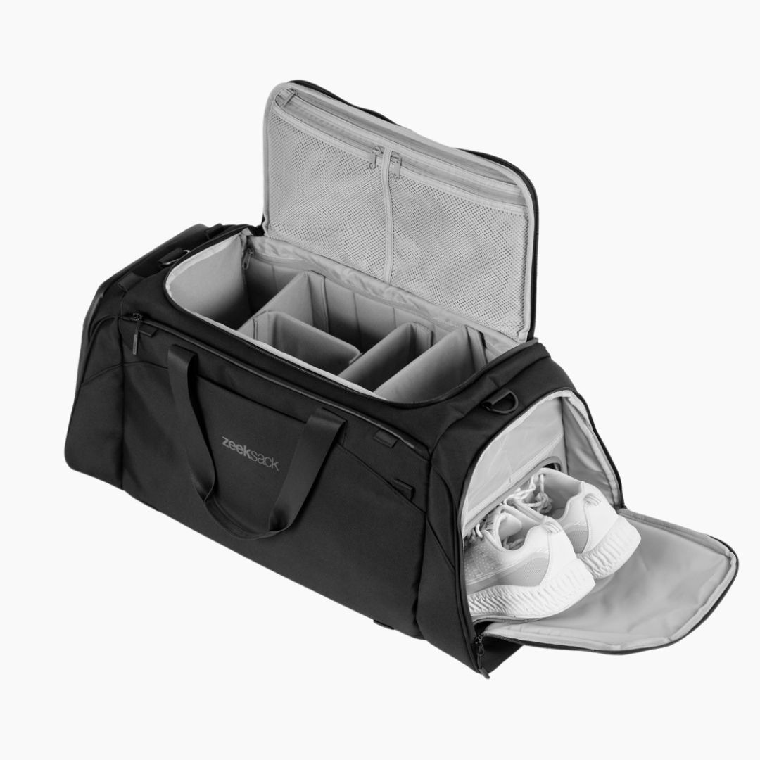Musta duffelilaukku, jossa järjestetyt lokerot ja erillinen kenkälokero valkoisilla kengillä.