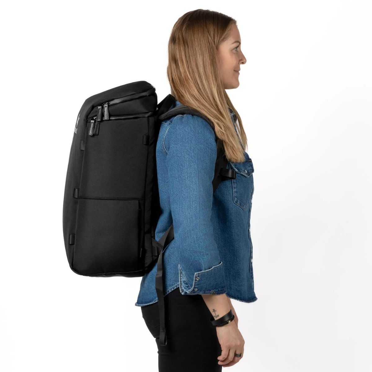 Nainen seisoo sivuprofiilissa ja kantaa mustaa Zeeksack-reppua.