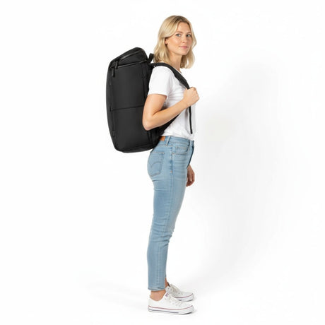 Nainen valkoisessa t-paidassa ja farkuissa kantaa mustaa Zeeksack-reppua, sivulta nähtynä.